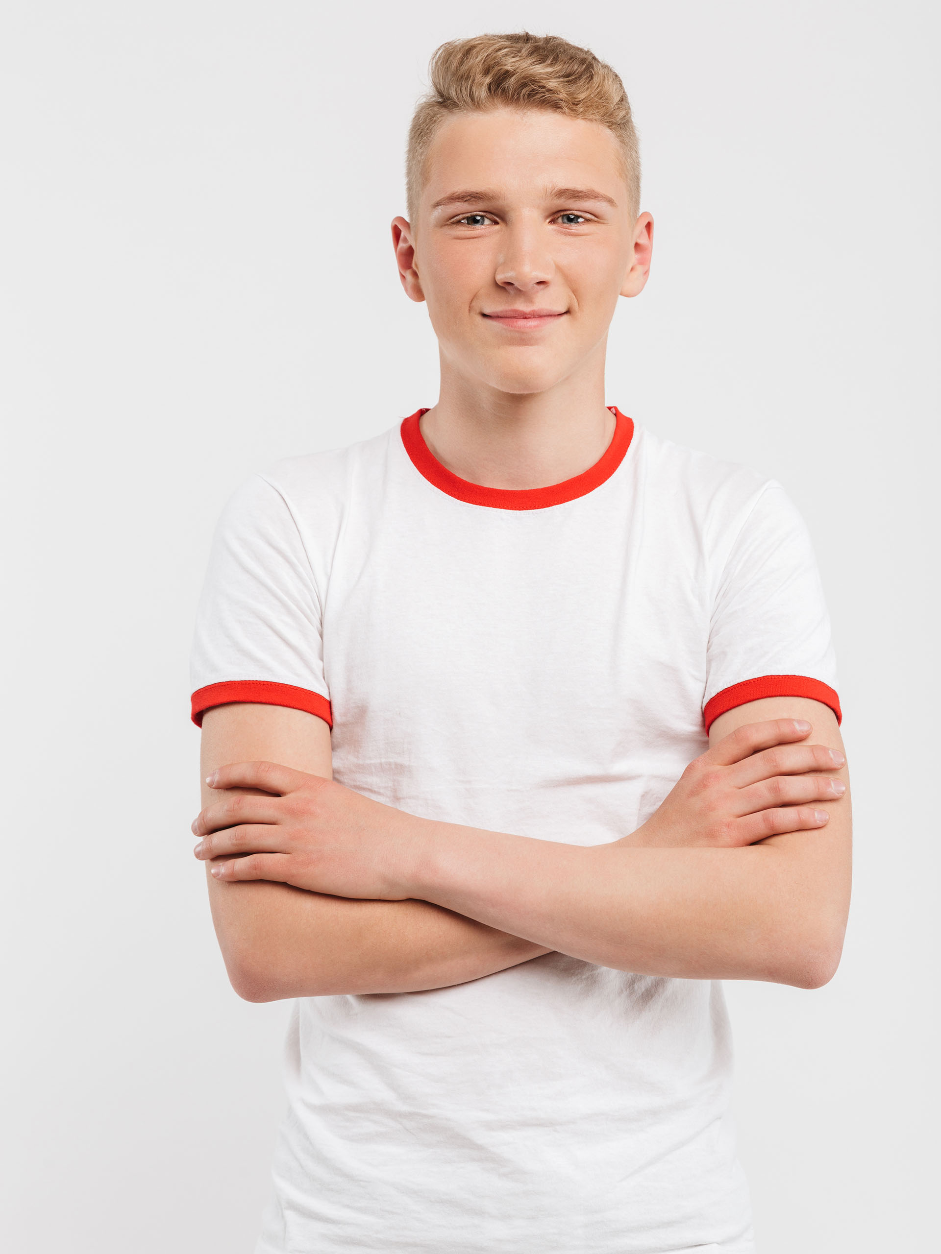 Portrait of a smiling teenage boy standing with arms folded isolated over white background